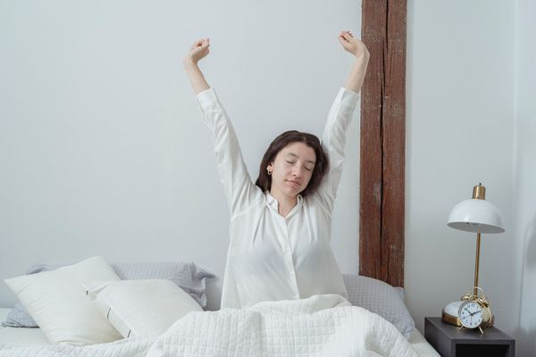 A woman stretching as she wakes up rested in a bright bedroom